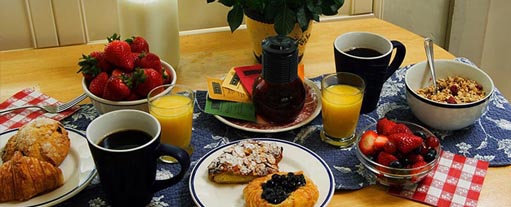 An image a table containing cofee, croissants, strawberries, orange juice, cerials, a bowl of fruit and some milk.